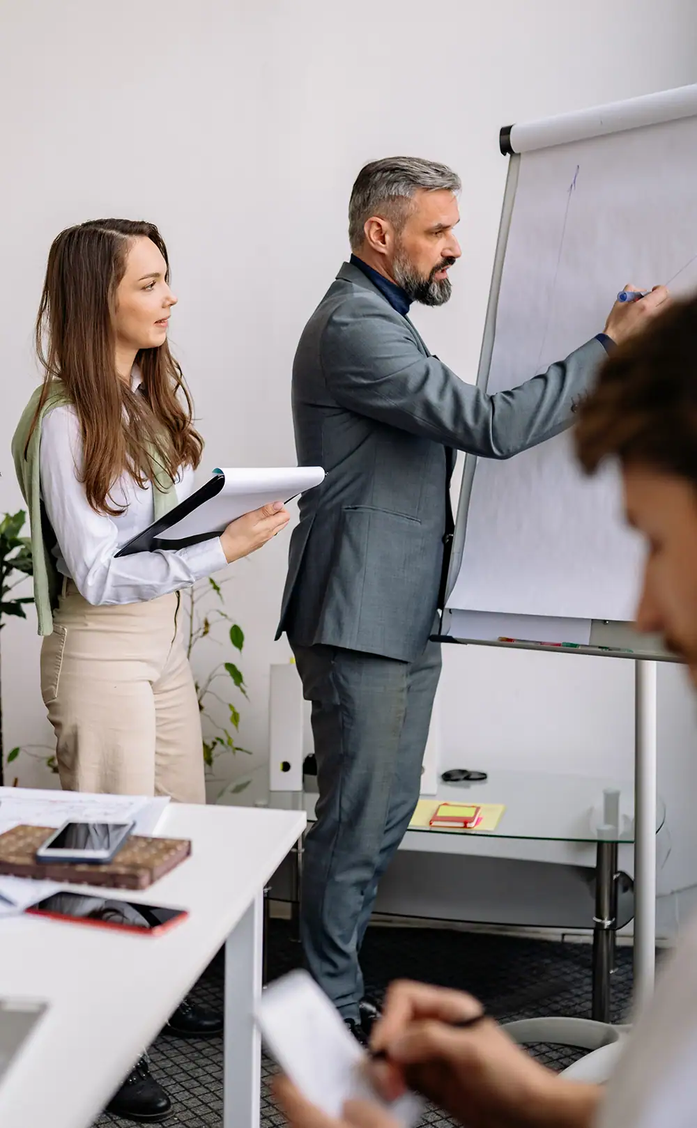 Eine Frau und ein Mann stehen vor einem Flipchart. Der Mann schreibt etwas auf